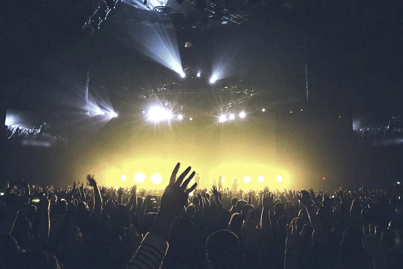 Concert crowd with hands raised under stage lights